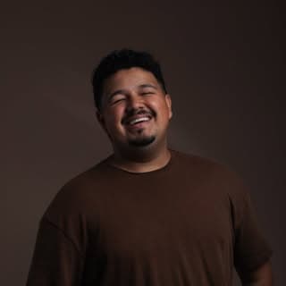 Doug sorrindo, de camiseta marrom, em retrato de estúdio